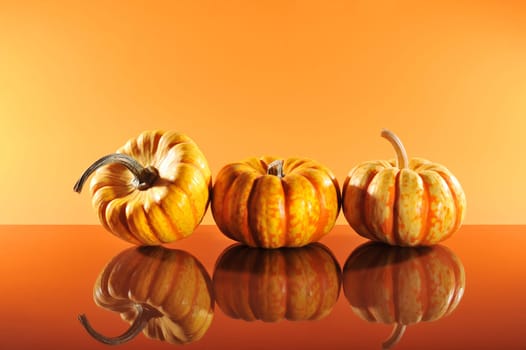 Three Halloween pumpkins on orange mirrored ground