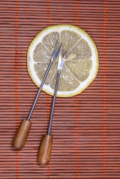 Sliced fresh lemon with forks on a nice wicker carpet as background