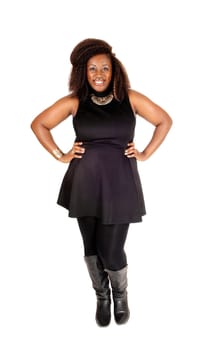 A pretty African American woman standing in a black dress, tights and boots.smiling isolated for white background..