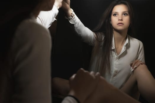 Low key portrait of young woman looking at her reflection in the mirror in a beam of light. Horizontally.