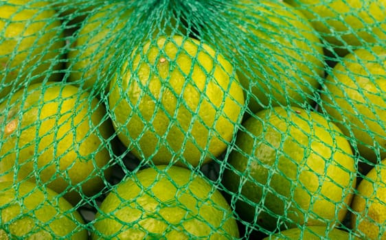 Fresh limes in the net green lime citrus fruit stand fullframe background.