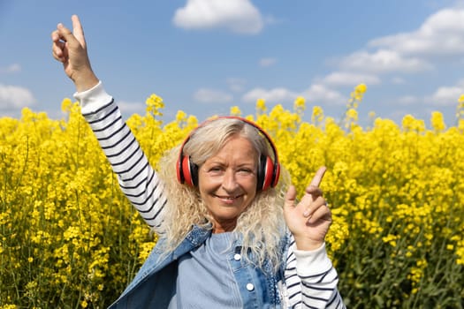 Elderly Woman listen to music with headphones in blooming canola field