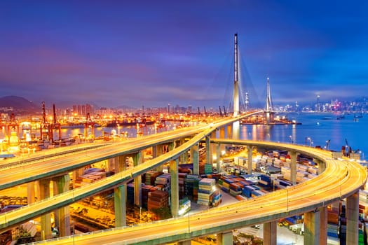 Container Cargo freight ship with working crane bridge in shipyard under Stonecutters highway bridge at sunset for Logistic Import Export, Hong kong