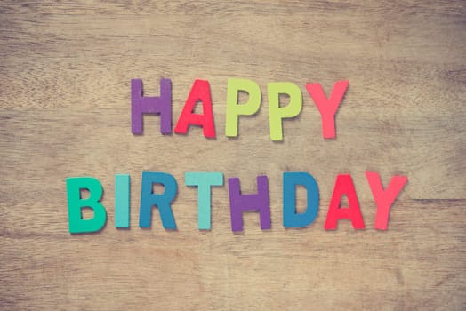 The colorful words "HAPPY BIRTHDAY"" made with wooden letters on old wooden plank."
