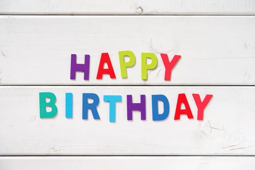 The colorful words "HAPPY BIRTHDAY"" made with wooden letters on white board."