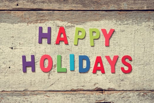 The colorful words "HAPPY HOLIDAYS"" made with wooden letters on wood board."