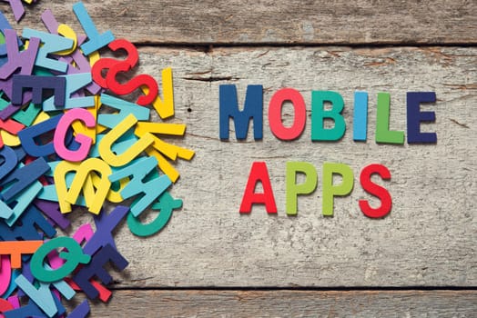 The colorful words "MOBILE APPS"" made with wooden letters next to a pile of other letters over old wooden board."