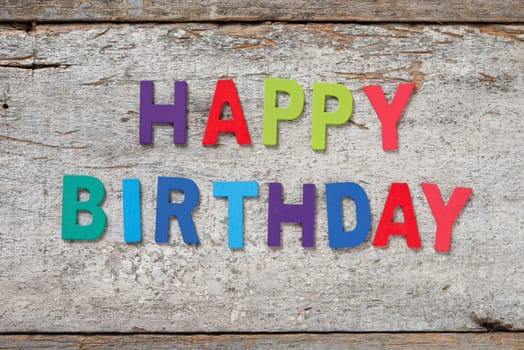 The colorful words "HAPPY BIRTHDAY"" made with wooden letters on old wooden board."