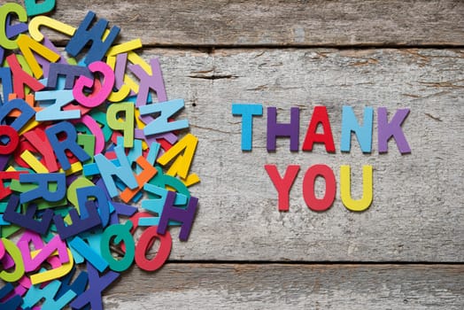 The colorful words "THANK YOU"" made with wooden letters next to a pile of other letters over old wooden board."