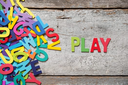 The colorful words "PLAY"" made with wooden letters next to a pile of other letters over old wooden board."