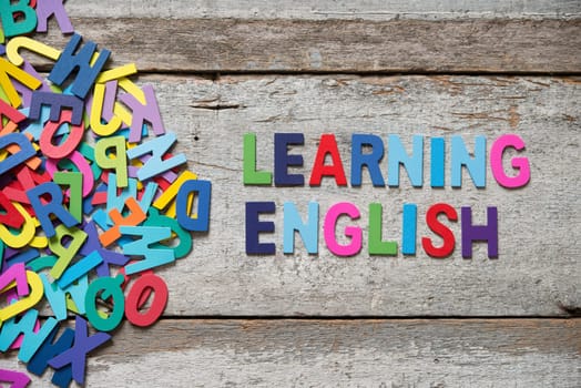 The colorful words "LEANRING ENGLISH"" made with wooden letters next to a pile of other letters over old wooden board."