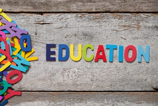 The colorful words "EDUCATION"" made with wooden letters next to a pile of other letters over old wooden board."