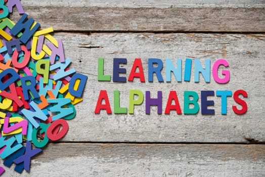 The colorful words "LEANRING ALPHABET"" made with wooden letters next to a pile of other letters over old wooden board."