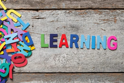 The colorful words "LEARNING"" made with wooden letters next to a pile of other letters over old wooden board."