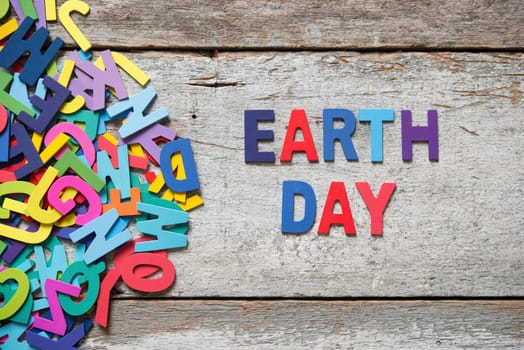 The colorful words "EARTH DAY"" made with wooden letters next to a pile of other letters over old wooden board."