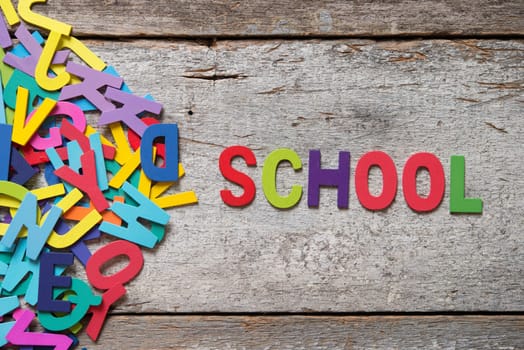 The colorful words "SCHOOL"" made with wooden letters next to a pile of other letters over old wooden board."