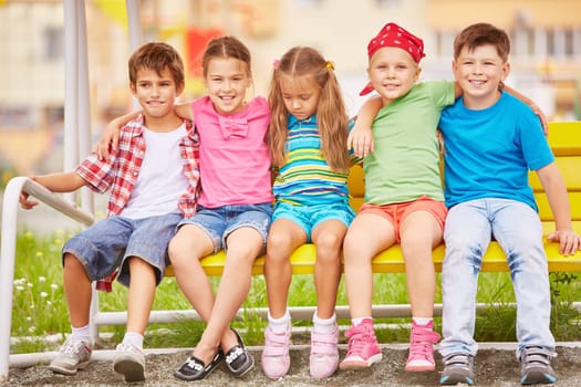 Group of friendly kids sitting on bench outside