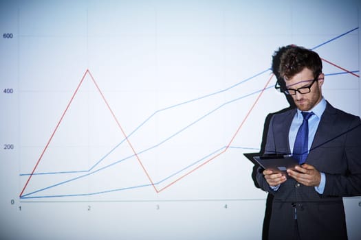 Serious businessman with touchpad standing by wall with graph