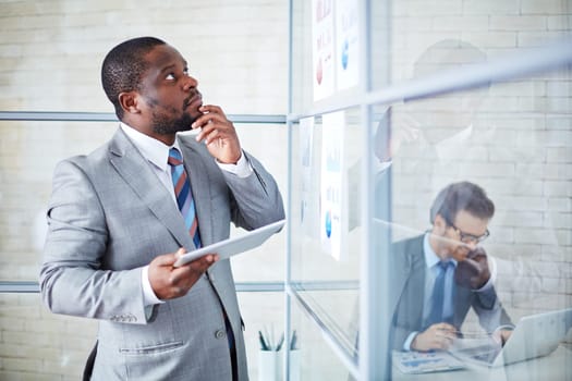 Pensive businessman with touchpad looking at documents in office