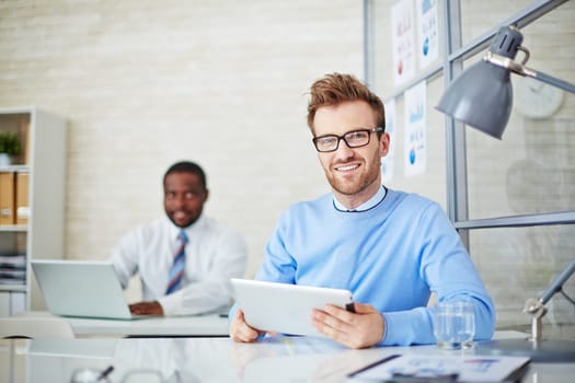 Young man with touchpad looking at camera during work in office