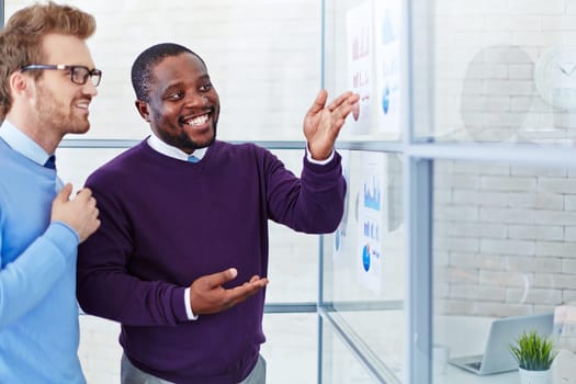 Male employee comparing financial data on papers and explaining it to colleague