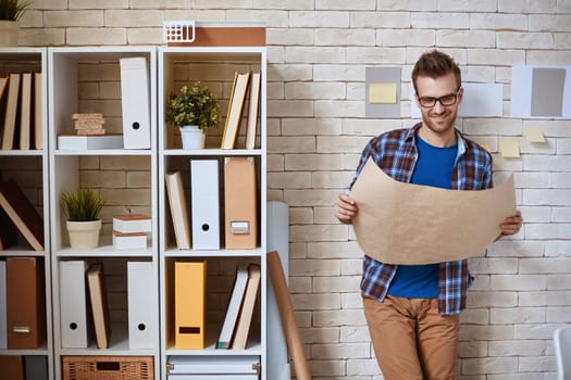 Young architect with blueprint standing by wall