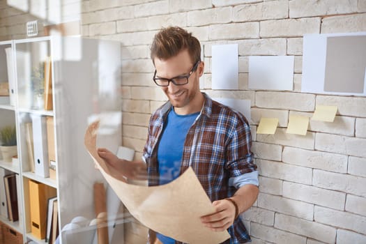 Young architect in casualwear reading document by the wall