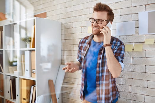 Young businessman standing by office wall and speaking on the cellphone