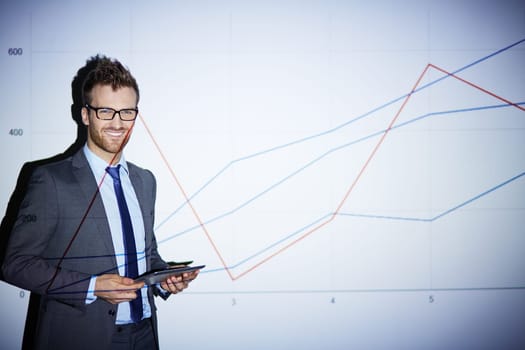 Smiling businessman with touchpad standing by wall with graph
