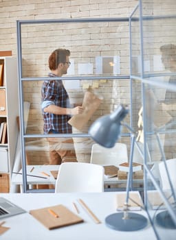 Young architect with blueprint standing by wall