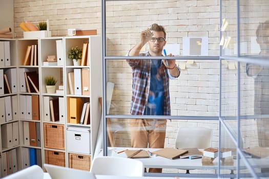 Serious businessman drawing graph on transparent board in office