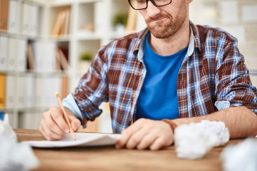 Young businessman with pencil writing down his ideas with crumpled sheets near by