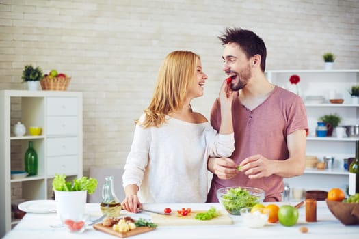 Happy female giving tomato to her husband while cooking salad