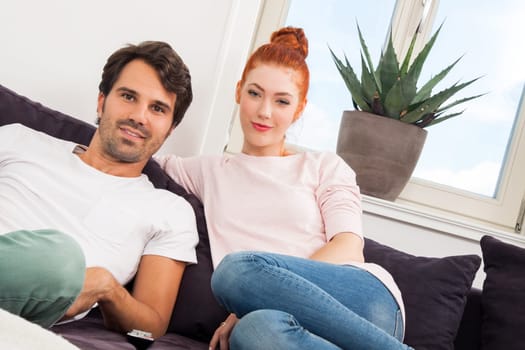 Young couple sits on the couch in the living room and looks away from home