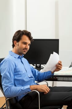 Young businessman sits with documents at a grater table in the office and informs himself