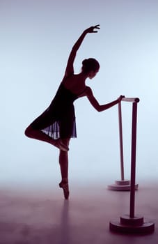 young ballerina stretching on the bar on blue background. The outline shooting - silhouette of girl