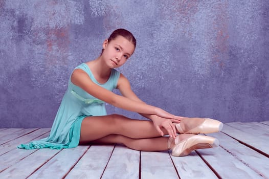 young ballerina sitting on wooden floor on a lilac background