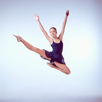 young ballet dancer jumping on a grey background. Ballerina is wearing in blue dress and pointe shoes