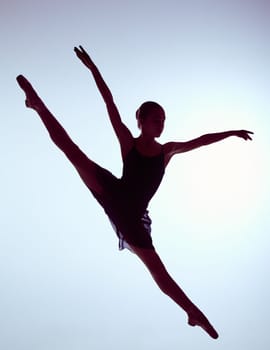 young ballet dancer jumping on a grey background. Ballerina is wearing in blue dress and pointe shoes. The outline shooting - silhouette of girl