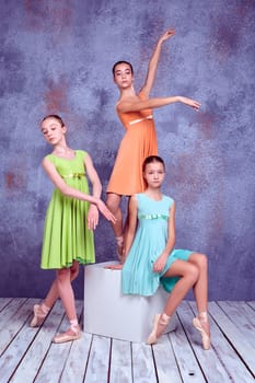 Three young ballerinas in colorful dresses posing on lilac wooden floor background