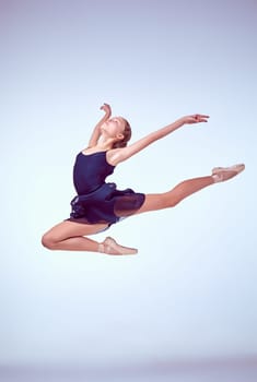 young ballet dancer jumping on a grey background. Ballerina is wearing in blue dress and pointe shoes