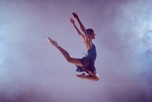 young ballet dancer jumping on a lilac background. Ballerina is wearing in blue dress and pointe shoes. The outline shooting - silhouette of girl with smoke effect