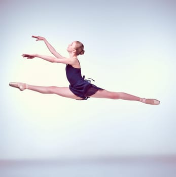 young ballet dancer jumping on a grey background. Ballerina is wearing in blue dress and pointe shoes
