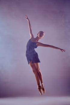 young ballet dancer jumping on a lilac background. Ballerina is wearing in blue dress and pointe shoes. The outline shooting - silhouette of girl with smoke effect