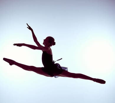 young ballet dancer jumping on a grey background. Ballerina is wearing in blue dress and pointe shoes. The outline shooting - silhouette of girl