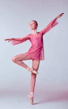 Young ballerina dancer in pink dress showing her techniques on lilac background
