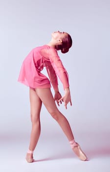 Young ballerina dancer in pink dress showing her techniques on gray background