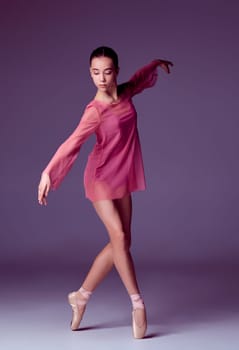 Young ballerina dancer in pink dress showing her techniques on lilac background