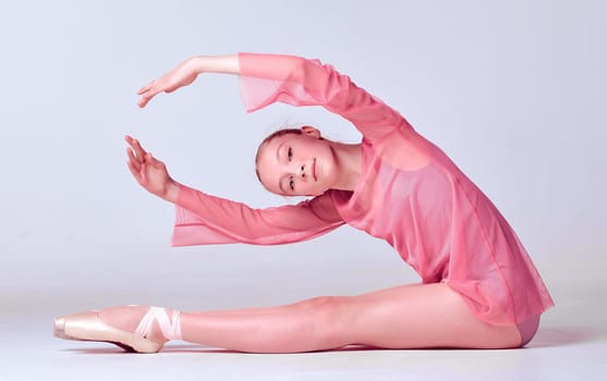 Young ballerina dancer in pink dress showing her techniques on lilac background