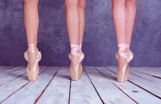 The close-up feet of a three young ballerinas in pointe shoes against the background of the wooden floor
